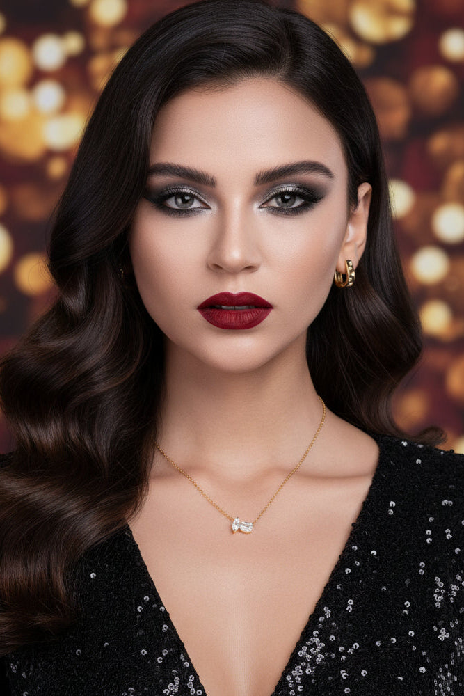Woman wearing gold jewelry including earrings, necklace, and ring on a plain background